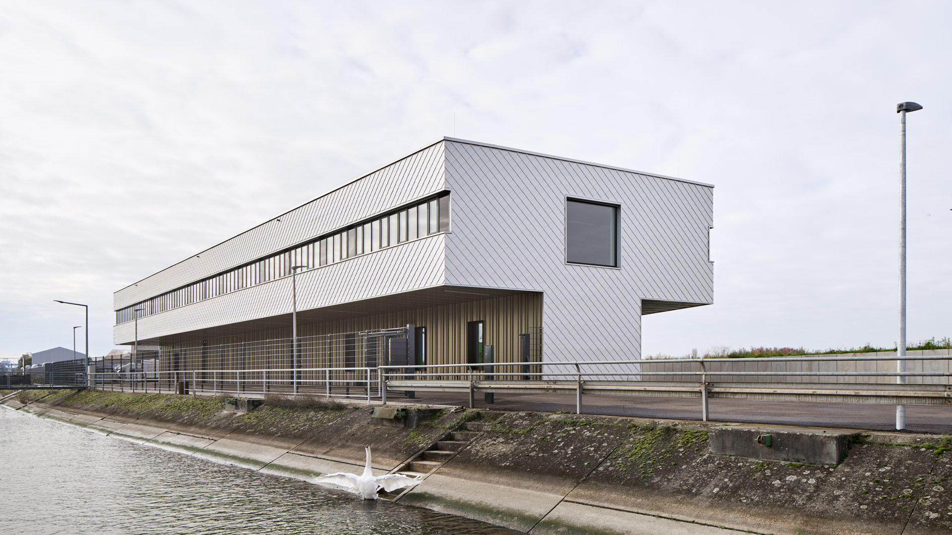 Außenansicht des Neubaus der Wasserschutzpolizei in Kehl am Rhein. Das zweigeschossige Gebäude mit metallischer Fassade liegt direkt am Wasser mit eigenem Bootssteg.