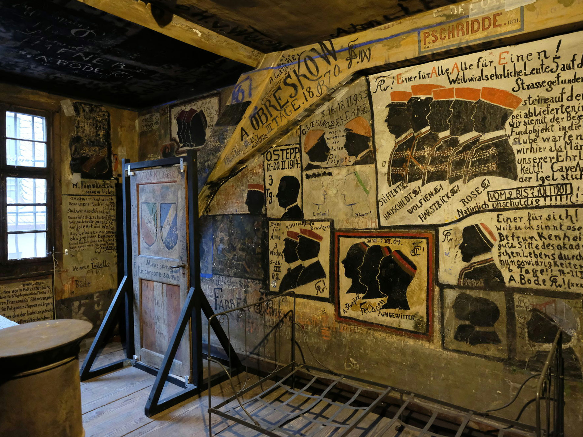 Ein historischer Raum mit Zeichnungen und Malereien an den Wänden. Mehrere Ausstellungsstücke, u. an. eine Tür in einem Gestell.