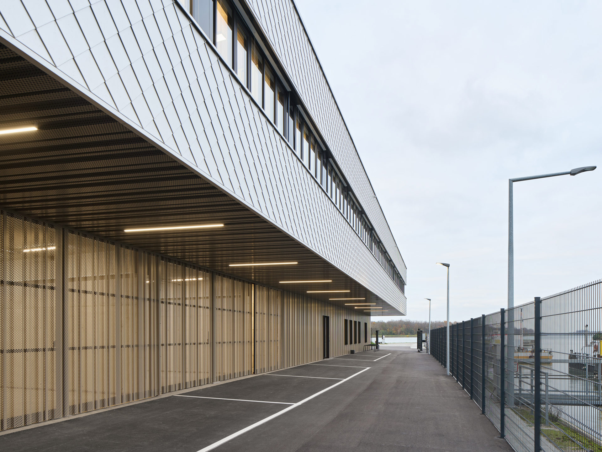 Neubau der Wasserschutzpolizei Kehl mit auskragendem Obergeschoss und Aluminiumschindeln mit schimmernder Oberfläche.