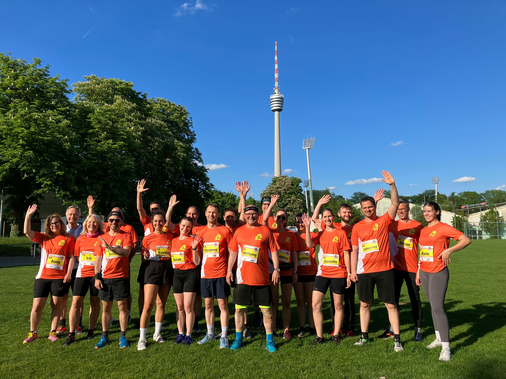 Gruppenbild: ca. 20 Personen in rotem Team-Dress winken teils in die Kamera, im Hintergrund der Stuttgarter Fernsehturm.