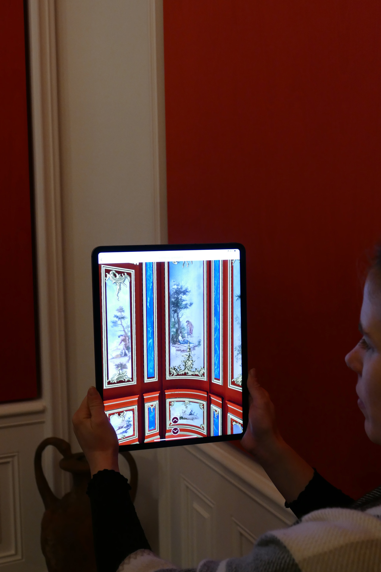 Eine Person blickt auf ein Display. Darauf sind die einfachen Wände, vor der sie steht, aufwändig bemalt dargestellt.