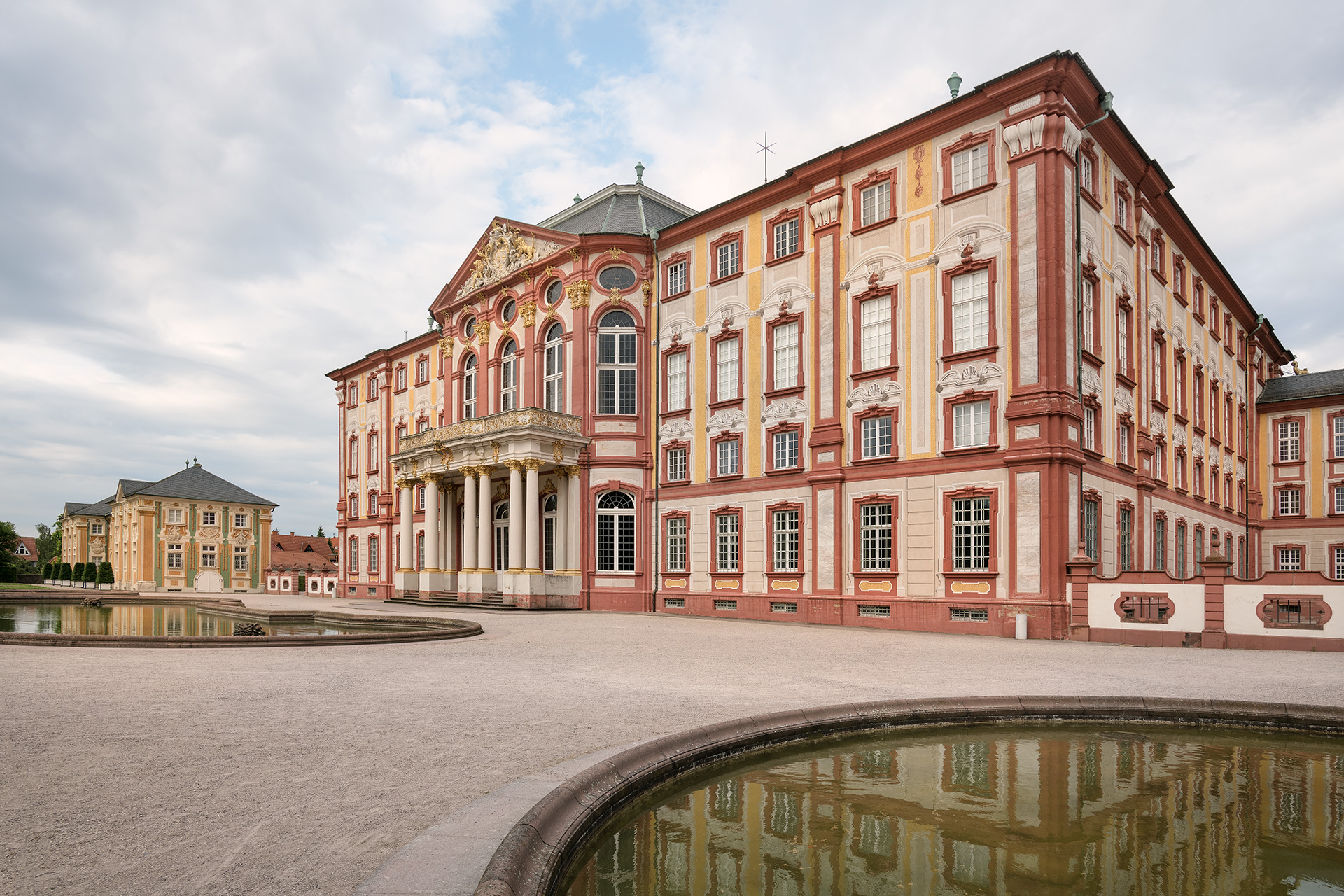 Barockes Schloss Bruchsal, von schräg links fotografiert; Wasser im Vordergrund spiegelt Teile der Fassade.