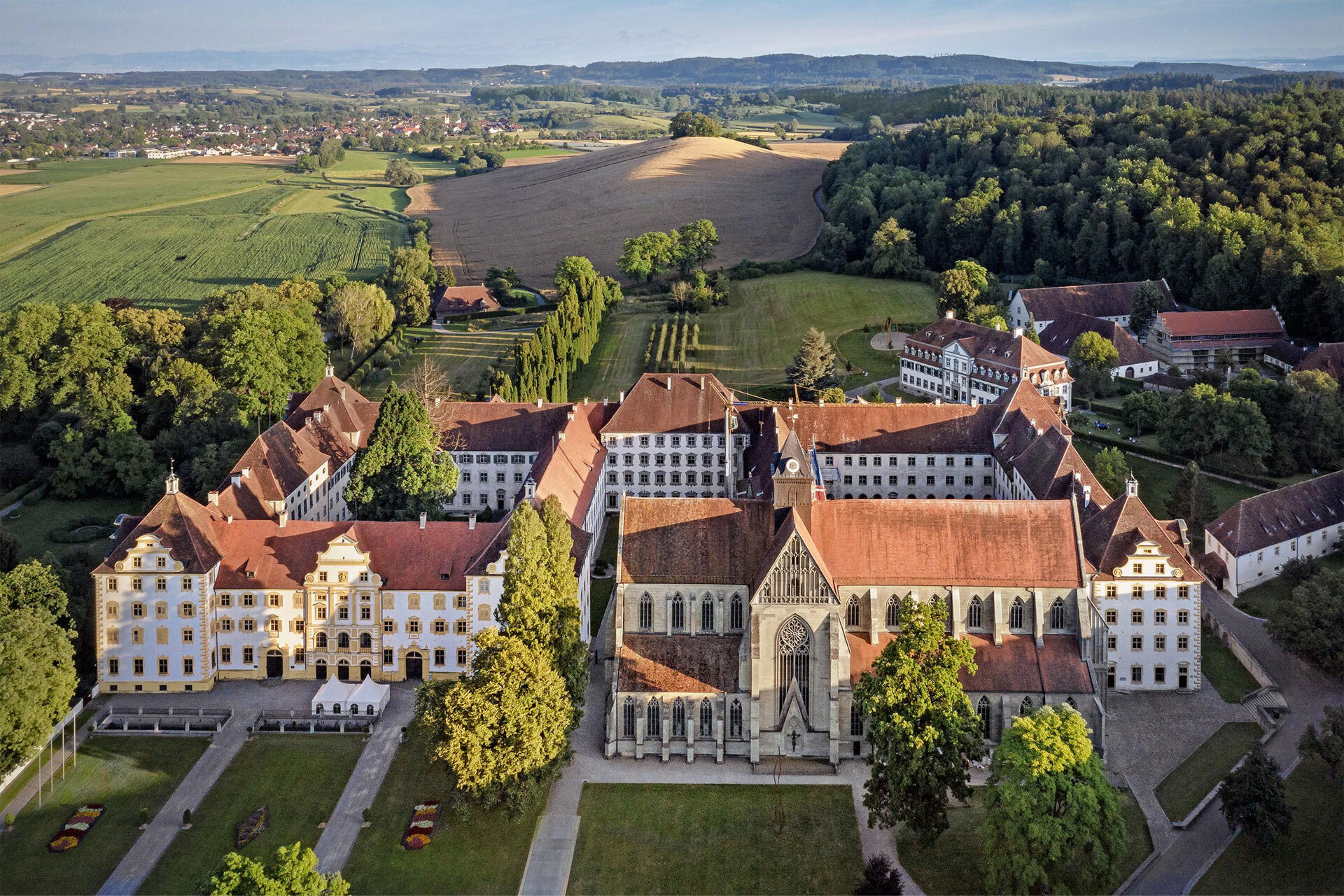 Blick aus der Vogelperspektive auf einen historischen Kloster- und Schlosskomplex, umgeben von Grünflächen, Bäumen, Äckern.