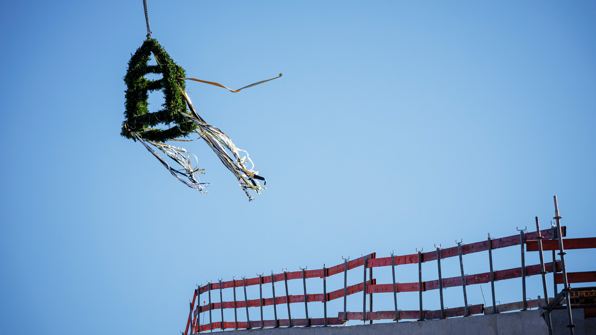 Eine Richtkrone mit im Wind wehenden Bändern über einem Bauzaun aus Holzplanken.