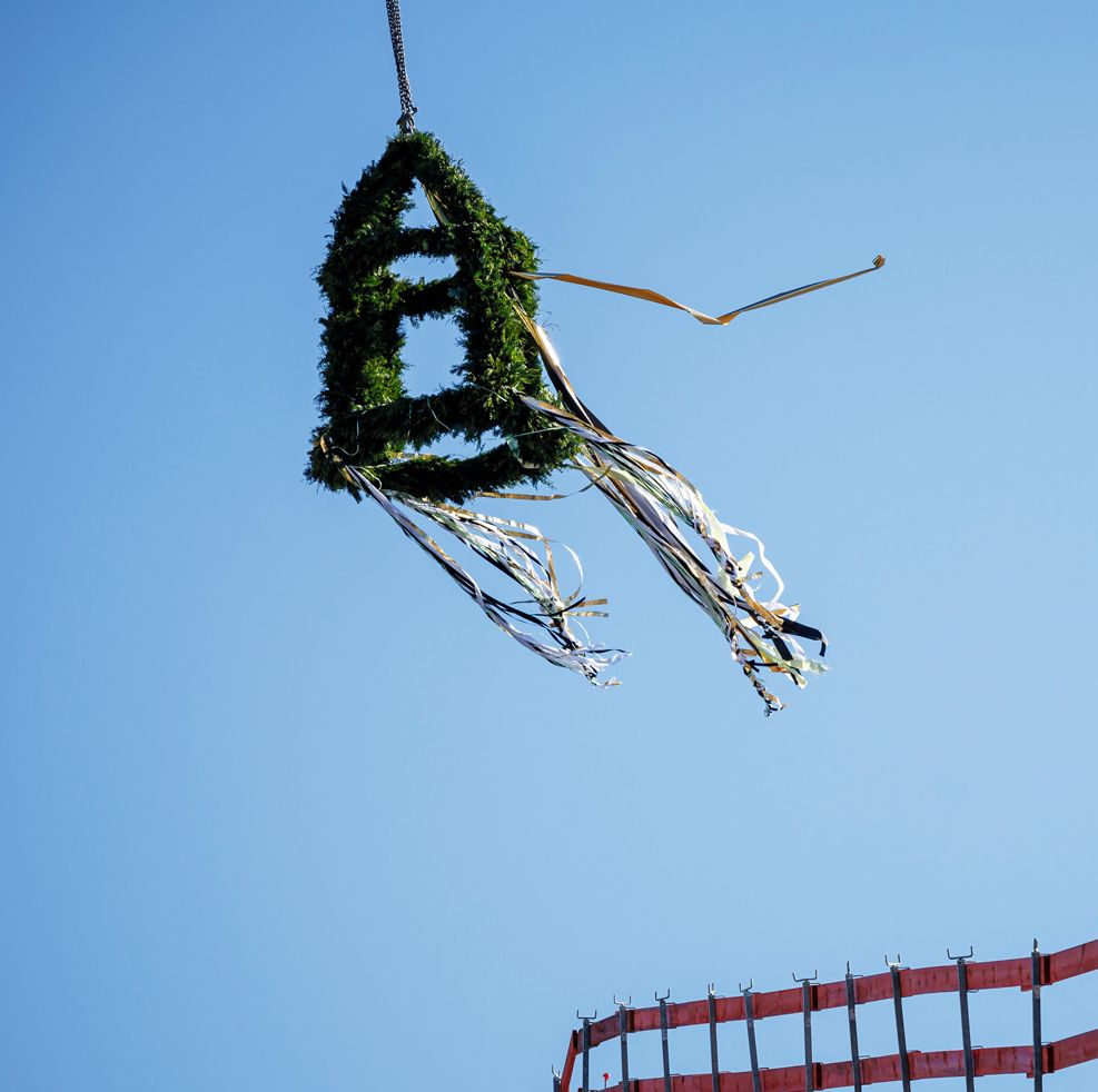 Eine Richtkrone mit im Wind wehenden Bändern über einem Bauzaun aus Holzplanken.