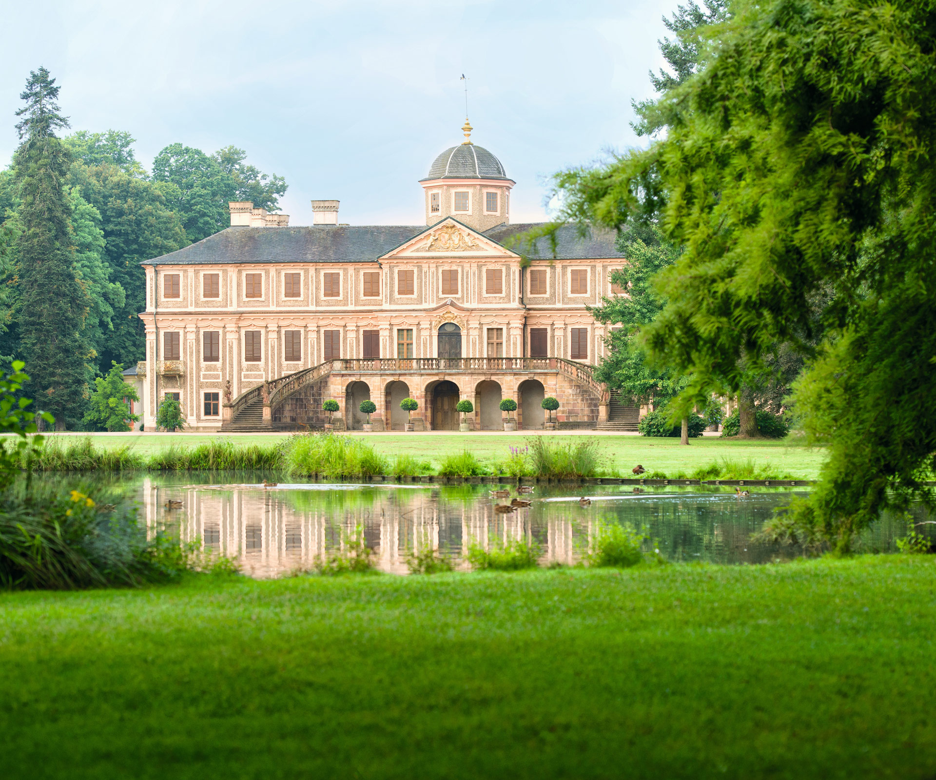 Blick zum Schloss Favorite Rastatt aus dem Schlossgarten mit Wasserfläche im Vordergrund.