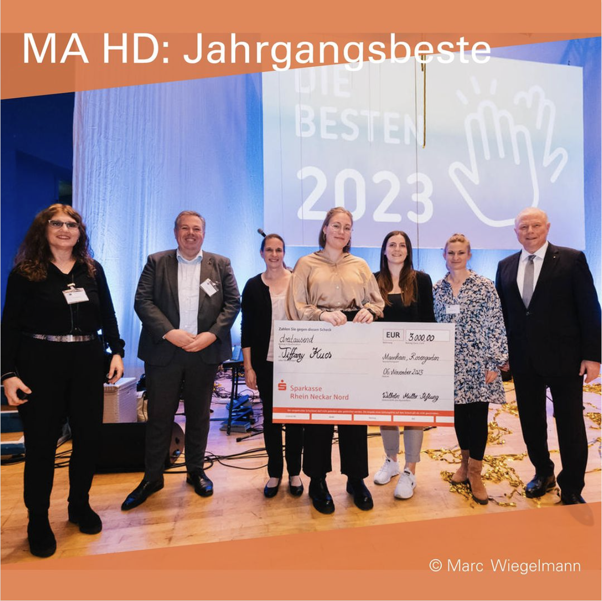 Auf einer Bühne stehen 7 Personen, eine hält einen überdimensionierten Scheck. Im Hintergrund steht: „Die Besten 2023“.