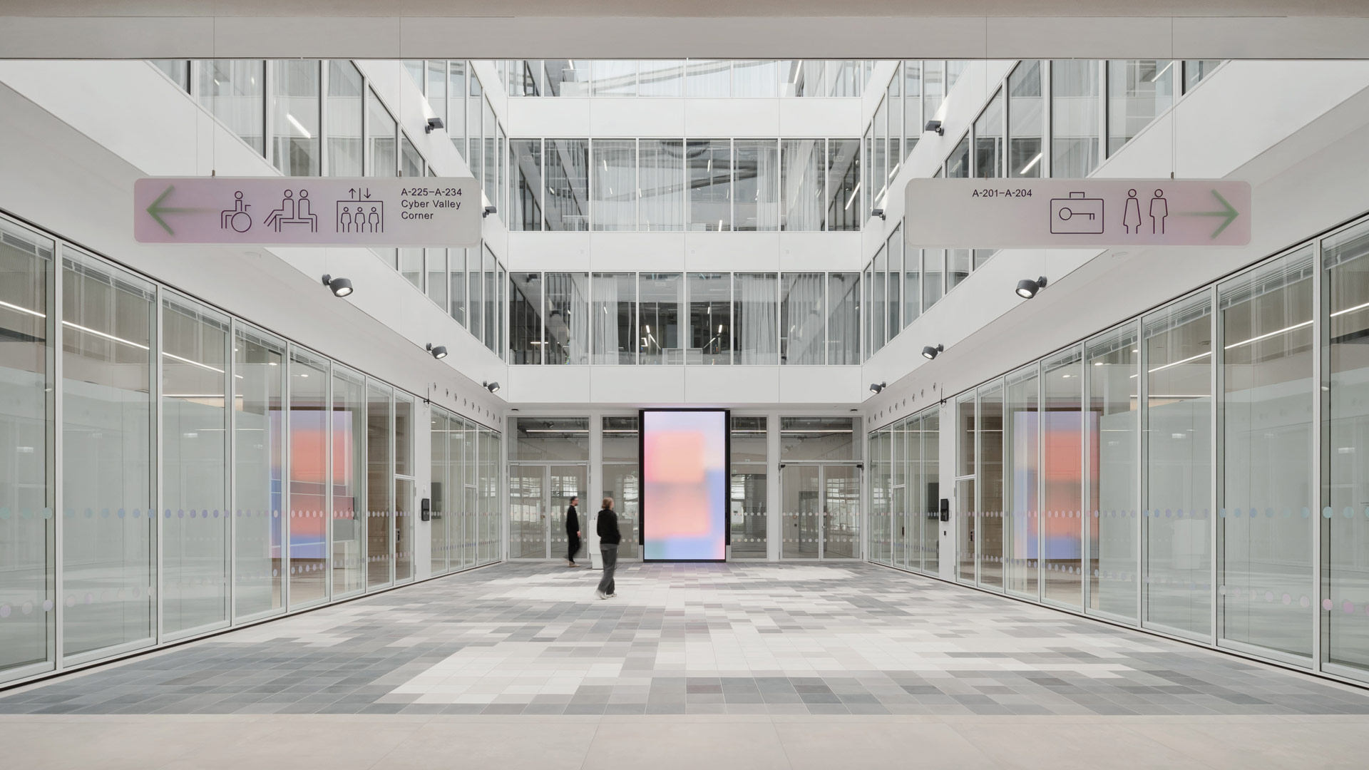 Helles Atrium mit weiß bis hellgrau gepflastertem Boden, gläsernen Wänden teils mit Sichtschutz und klar abgesetzten Geschossen.