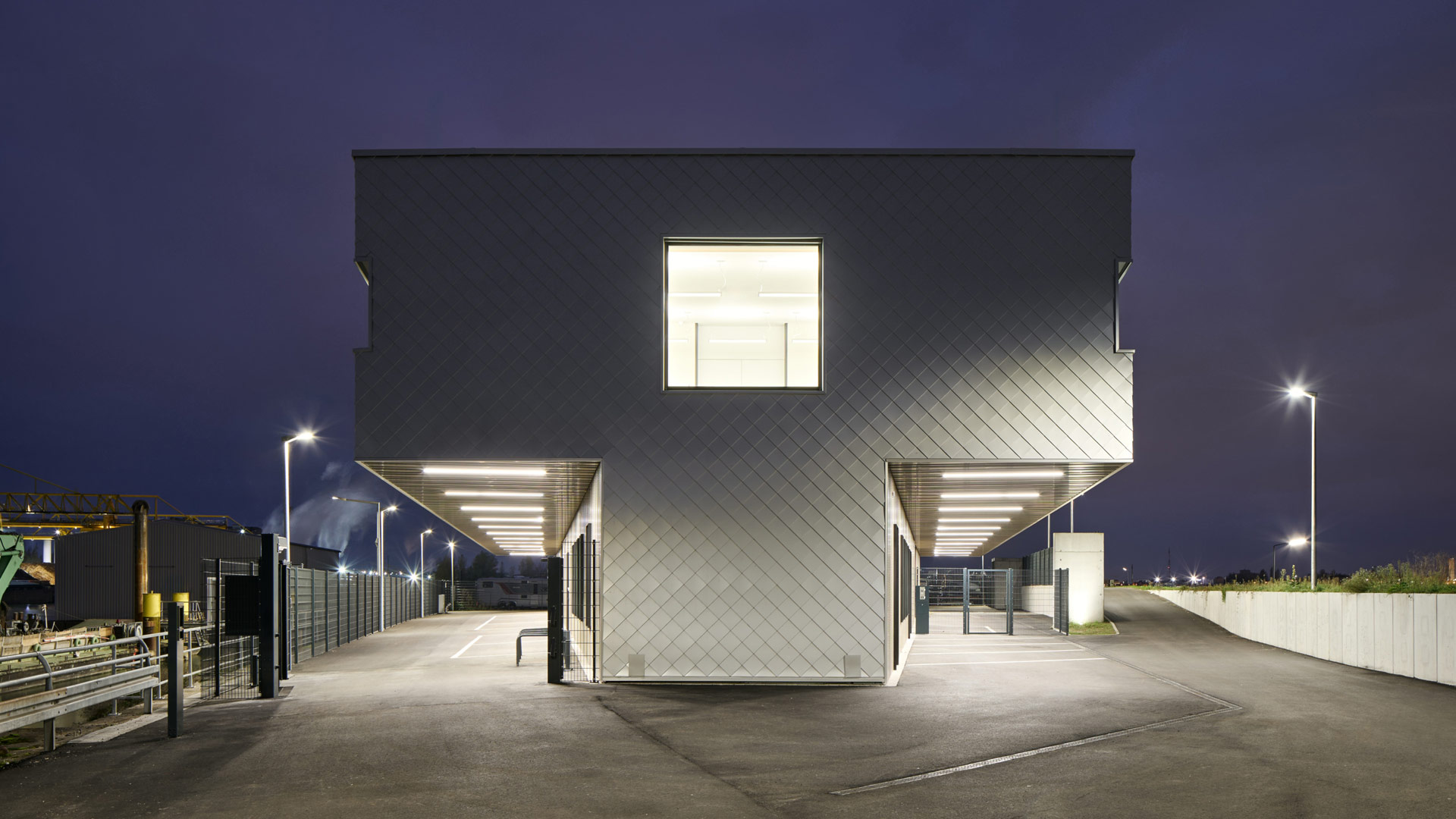 Nächtliche Ansicht des Neubaus der Wasserschutzpolizei Kehl mit beleuchteten Durchfahrten und markanter Metallfassade.