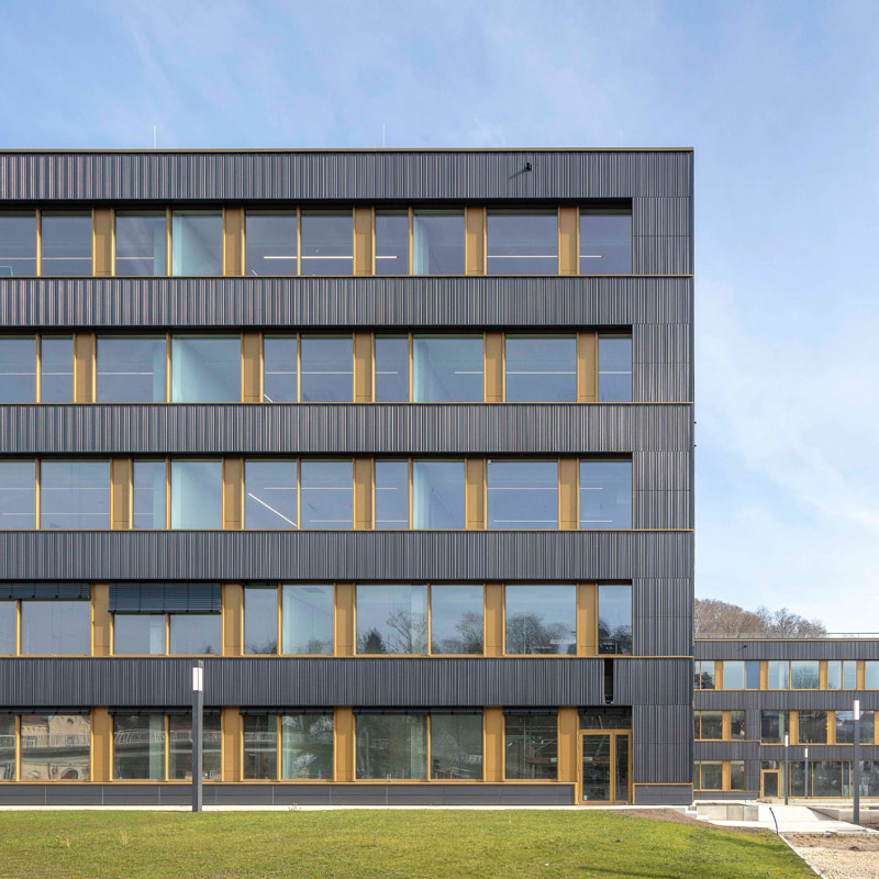 Modernes Gebäude der Dualen Hochschule Heidenheim mit goldenen Fensterrahmen und einer grünen Wiese im Vordergrund.