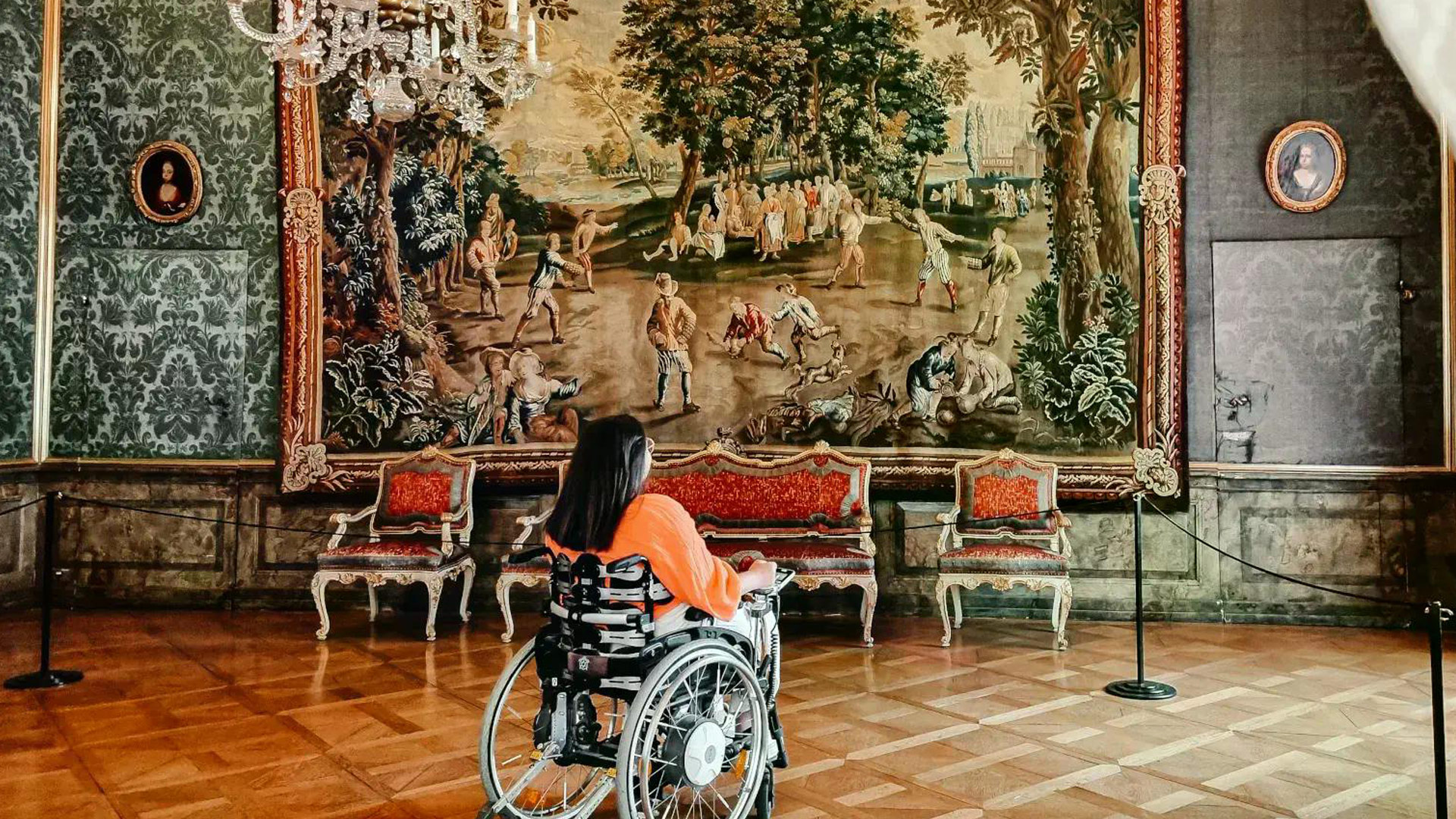 Person im Rollstuhl blickt auf Tapisserie.