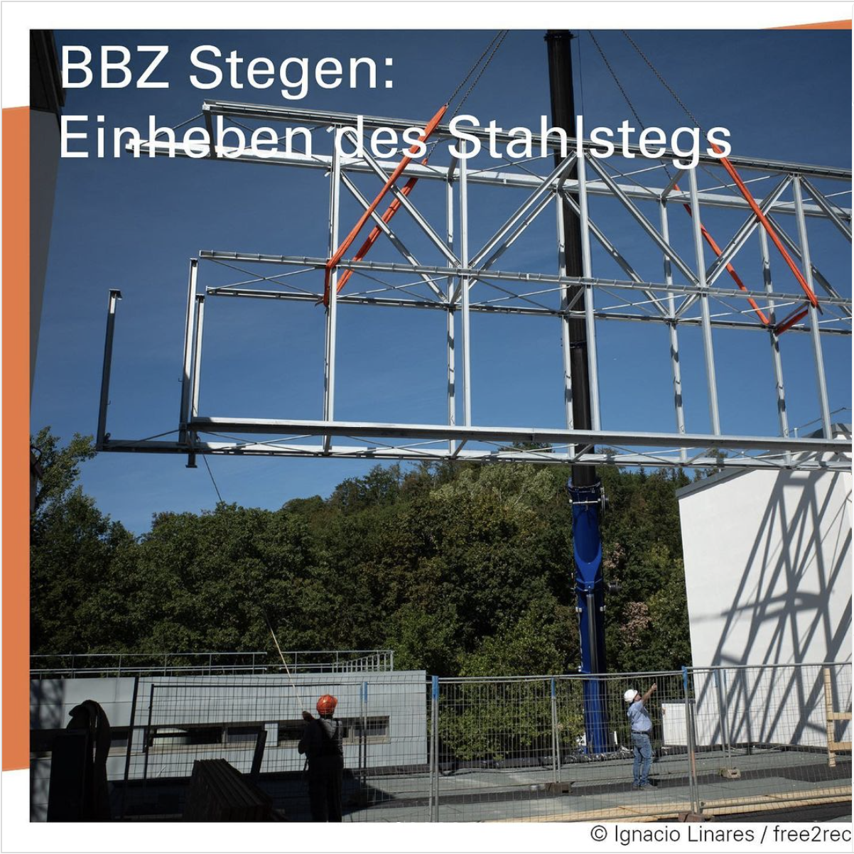 Zwei Bauarbeiter mit Helmen blicken nach oben auf eine über ihnen hängende eine Stahlrohrkonstruktion.