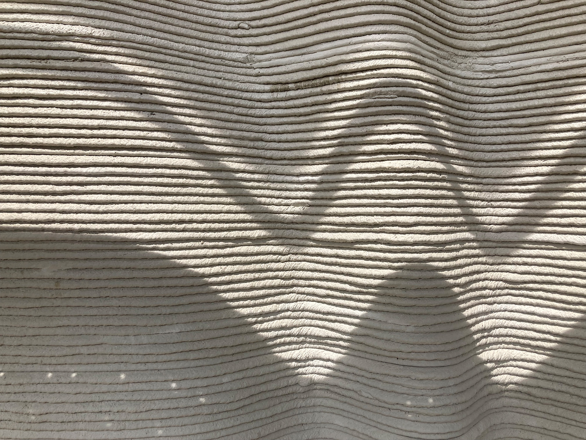 Eine geschwungene Wand, mit waagerechten, unregelmäßigen Rillen. Es ist nicht erkennbar, ob das Material hart oder weich ist.