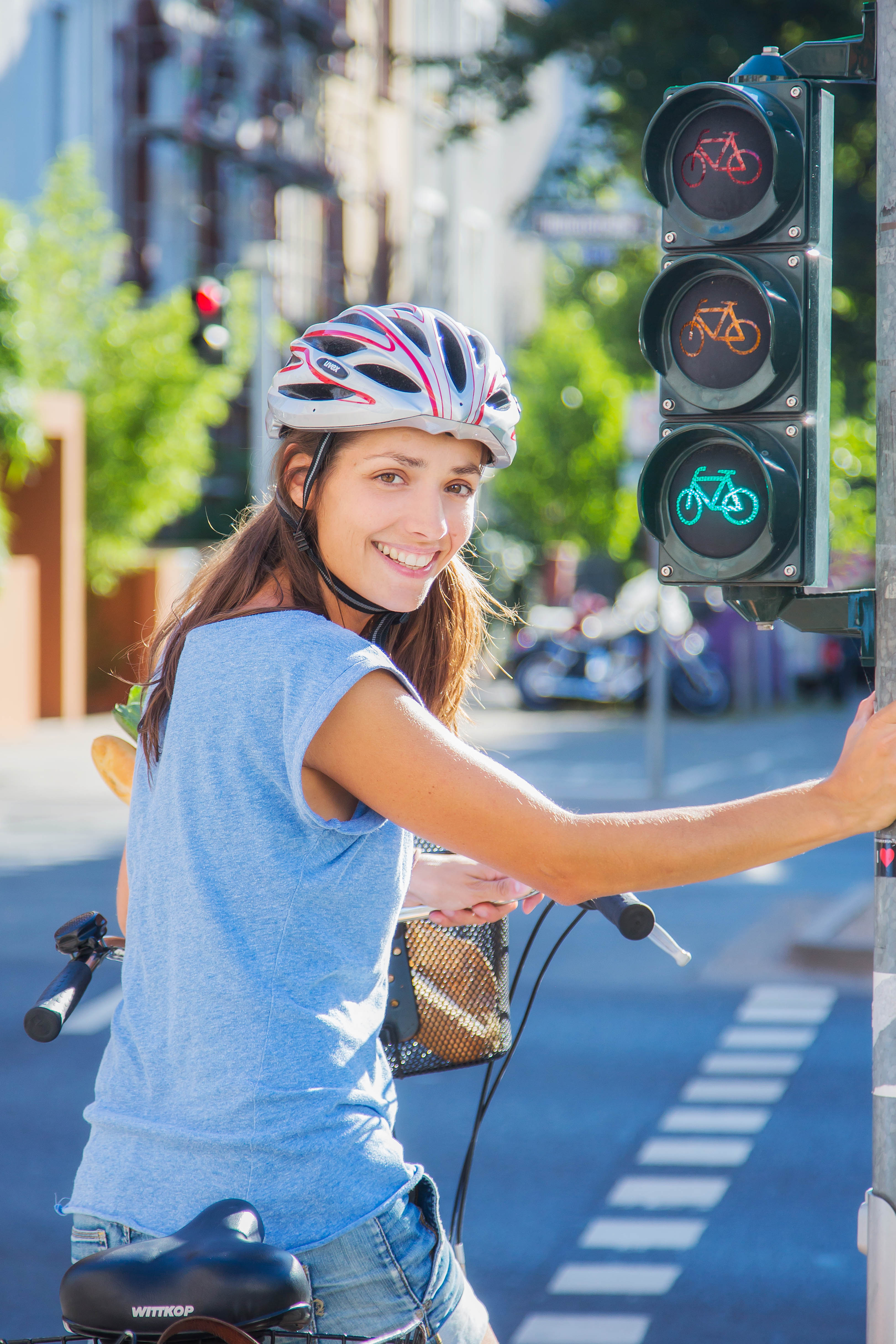 Eine Radfahrerin steht an einer grünen Ampel, hat sich zur Kamera umgedreht. Sie hat direkten Blickkontakt und lächelt. 