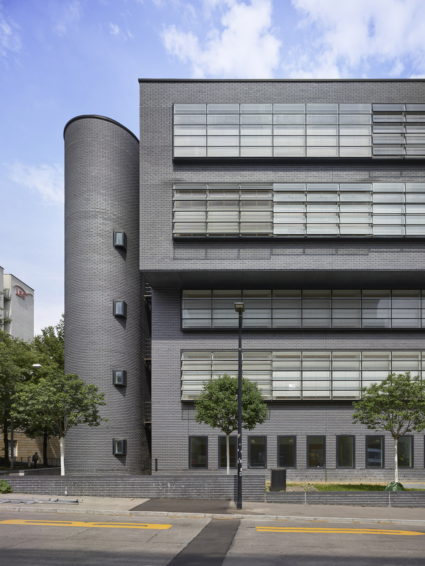 Ein mit kleinen grauen Steinen gemauertes Haus mit einem Turm links und kleinteiligen Fenstern, die zum Teil gekippt sind.