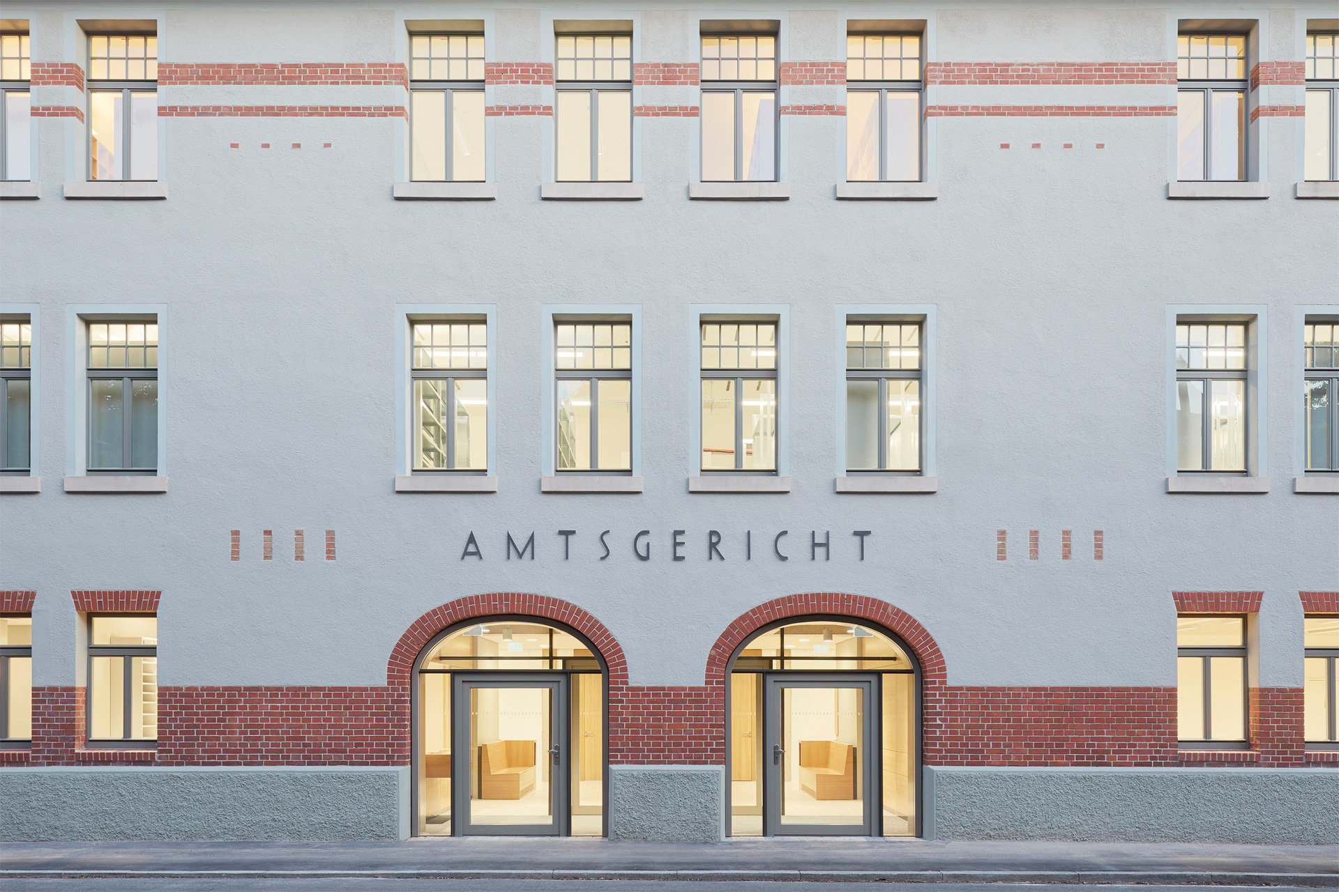 Eine graue Fassade. Über zwei verglasten, mit Klinkersteinen eingefasste Torbögen steht „Amtsgericht“.