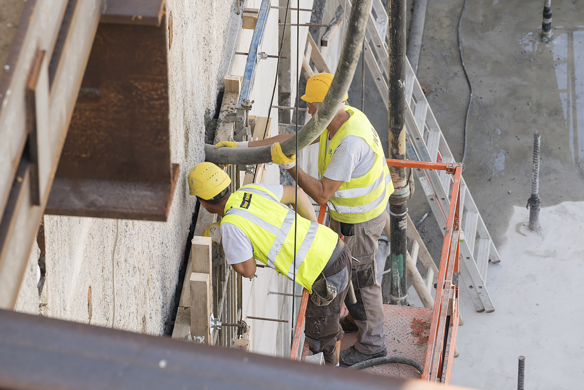Zwei Bauarbeiter mit gelben Helmen und Warnwesten machen sich auf einer Baustelle an einem Rohr zu schaffen.