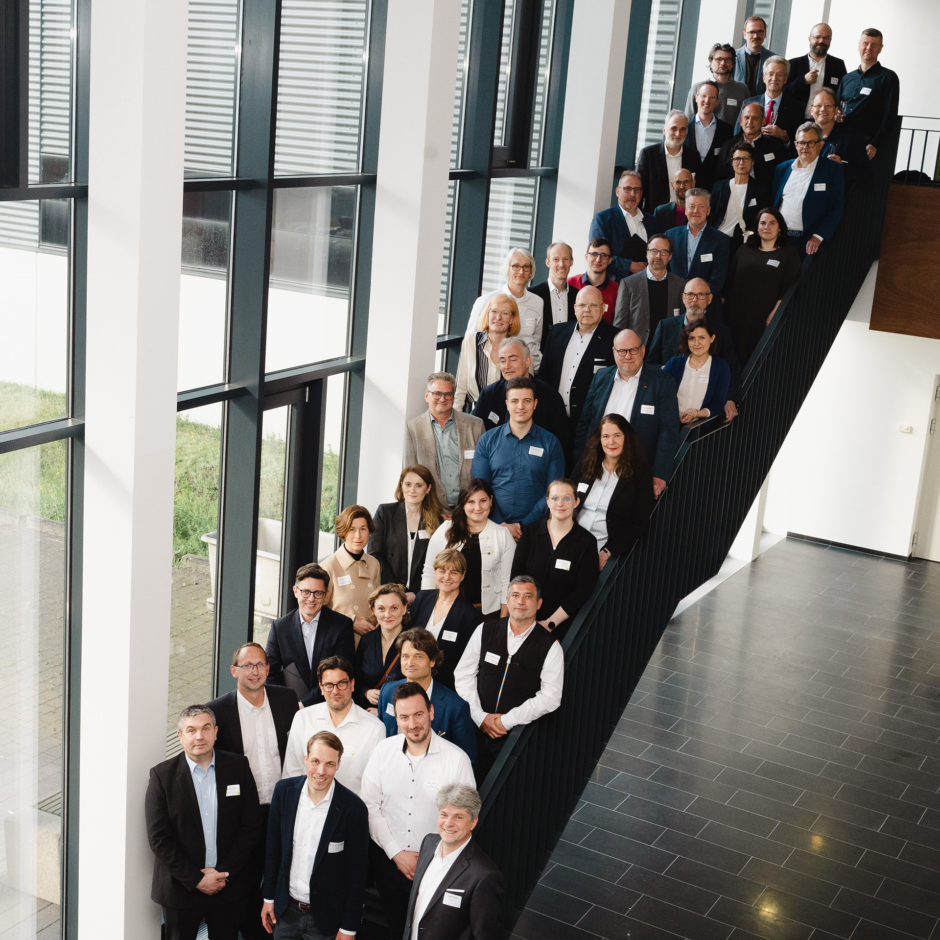 Gruppenbild: Ca. 40 Leute, jeder mit Namensschild, stehen auf einer schmalen Treppe und sind von schräg oben fotografiert.