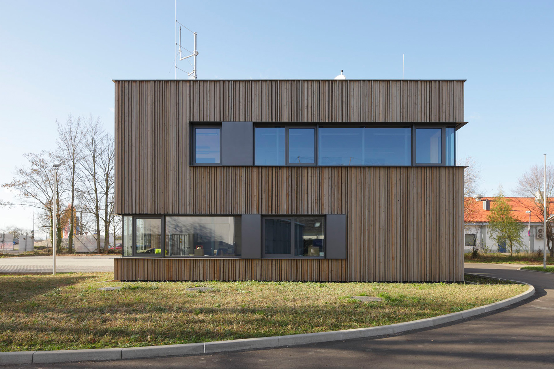 Ein zweigeschossiges Gebäude, die Fassade aus Holz mit großen Fensterflächen. Im Vordergrund eine kurz gemähte Rasenfläche.