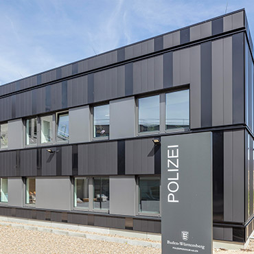 Ein flaches, modernes Gebäude der Polizeit. In unterschiedlichen Grautönen gehaltene Elemente an der Fassade.