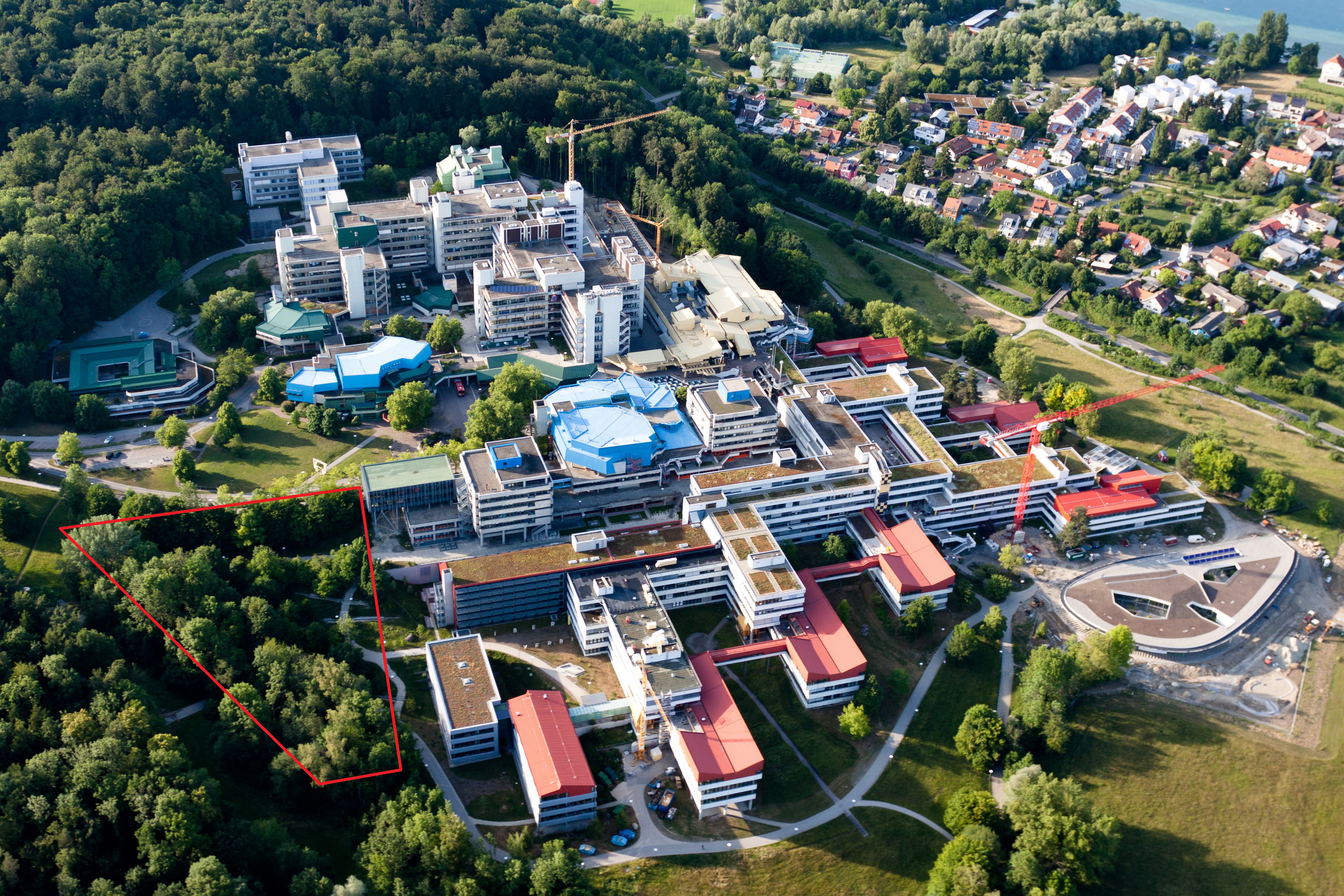 Vogelperspektive auf den Campus der Uni Konstanz: diverse Gebäude mit begrünten, aber auch mit roten und blauen Dachflächen.