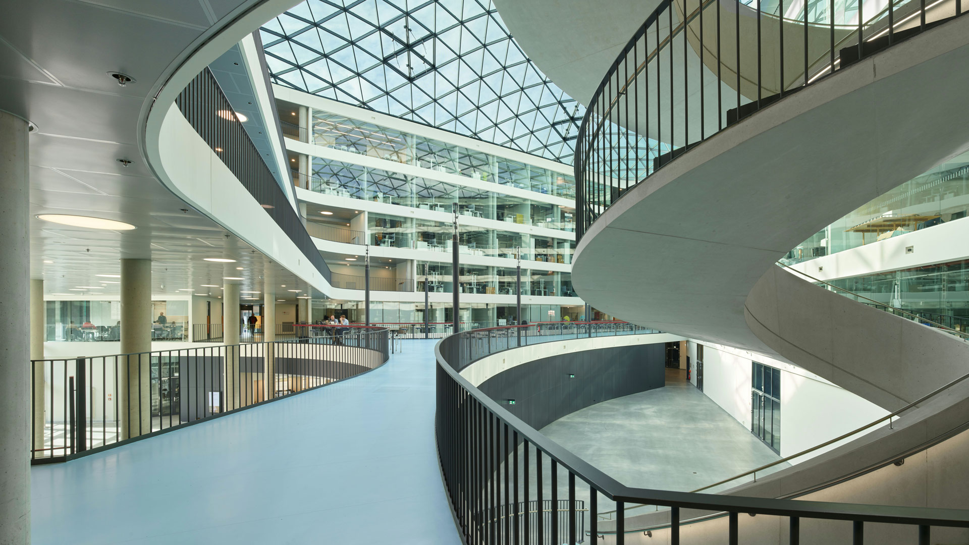 Innenraum-Perspektive des Neubaus der Dualen Hochschule Baden-Württemberg. Mehrstöckiges Atrium mit gewendelter Rampe, Glasdach und offenen Ebenen.