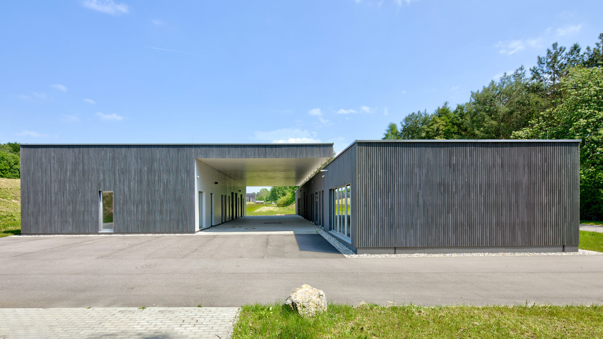 Ein flaches Gebäude mit zweiteiligem Baukörper, das einen mittigen, breiten Durchgang hat.