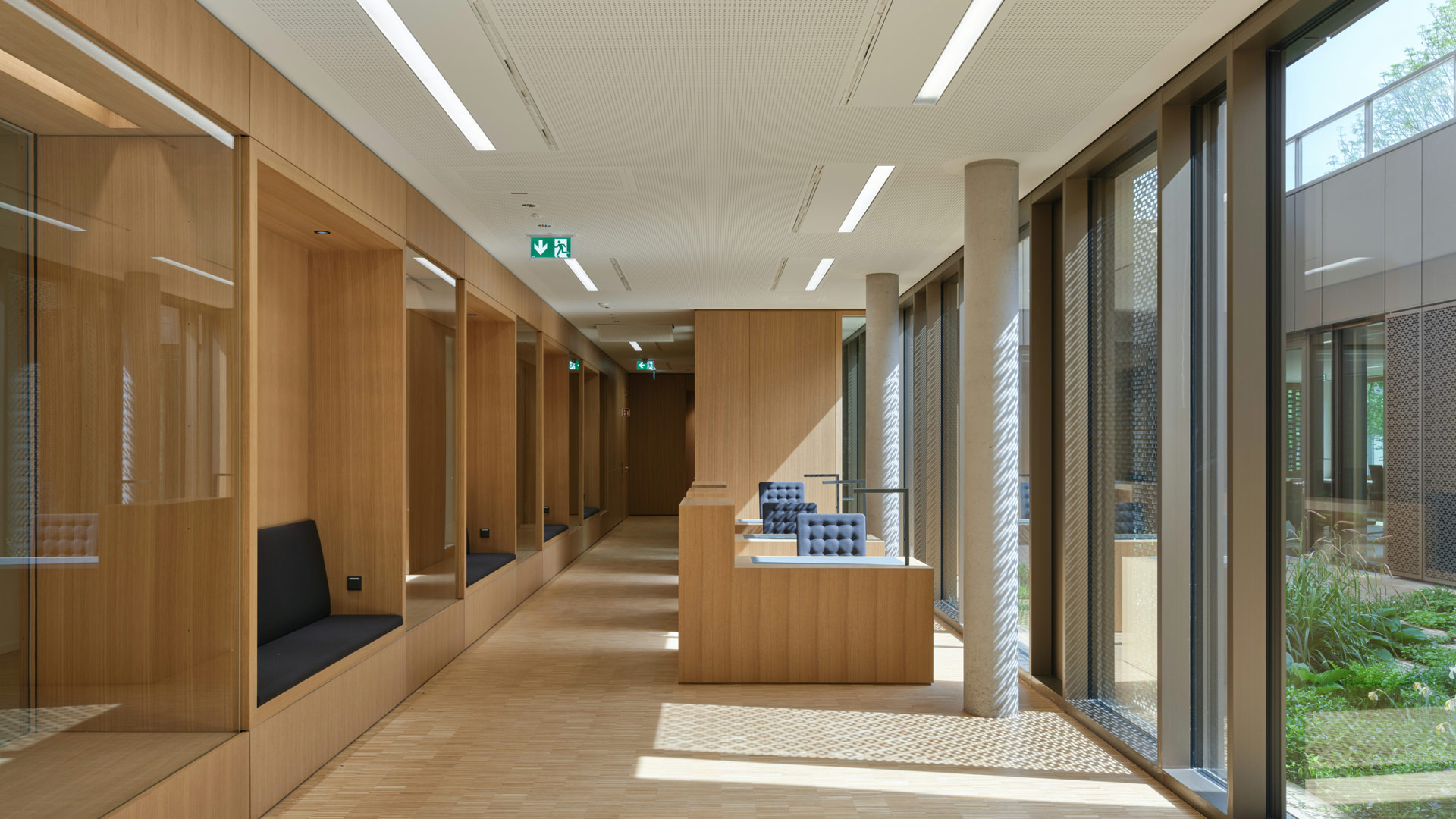 Ein Innenraum mit Holzboden und Arbeitstischen, links an der Wand Vitrinen und Sitzgelegenheiten, rechts eine Fensterfront.