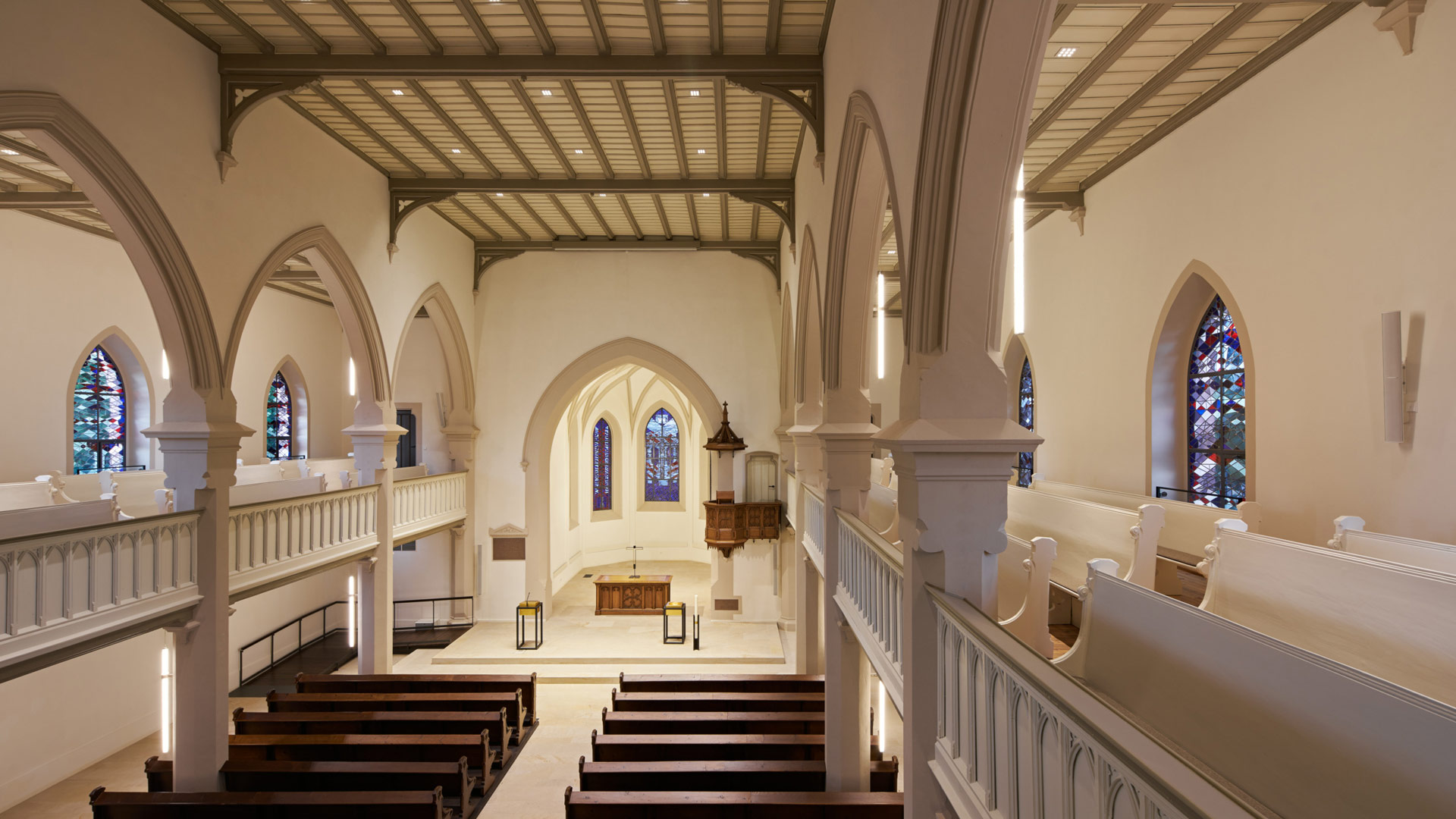 Der Innenraum einer Kirche mit dunklen Sitzbänken, ganz hinten klein der Altartisch.
