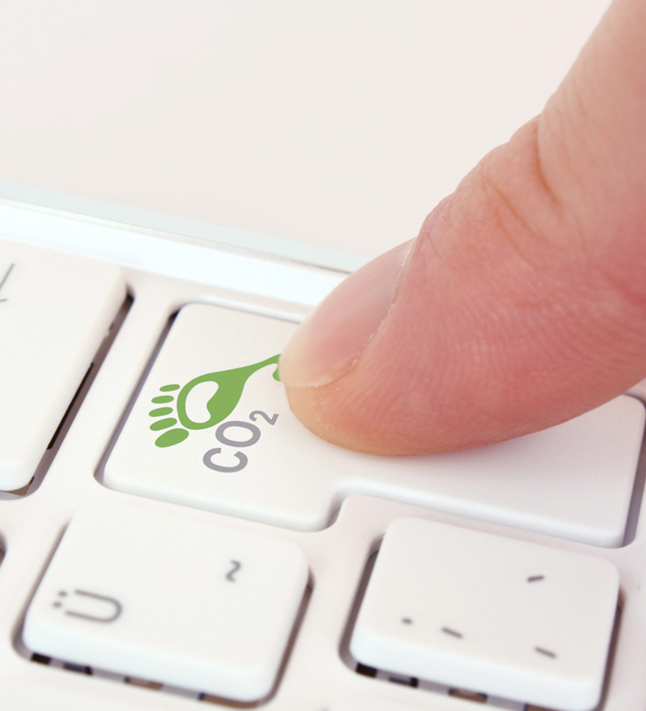 Nahaufnahme eines Fingers auf einer weißen Computertastatur. Die gedrückte Taste zeigt ein grünes Symbol eines Fußabdrucks mit der Beschriftung CO₂.