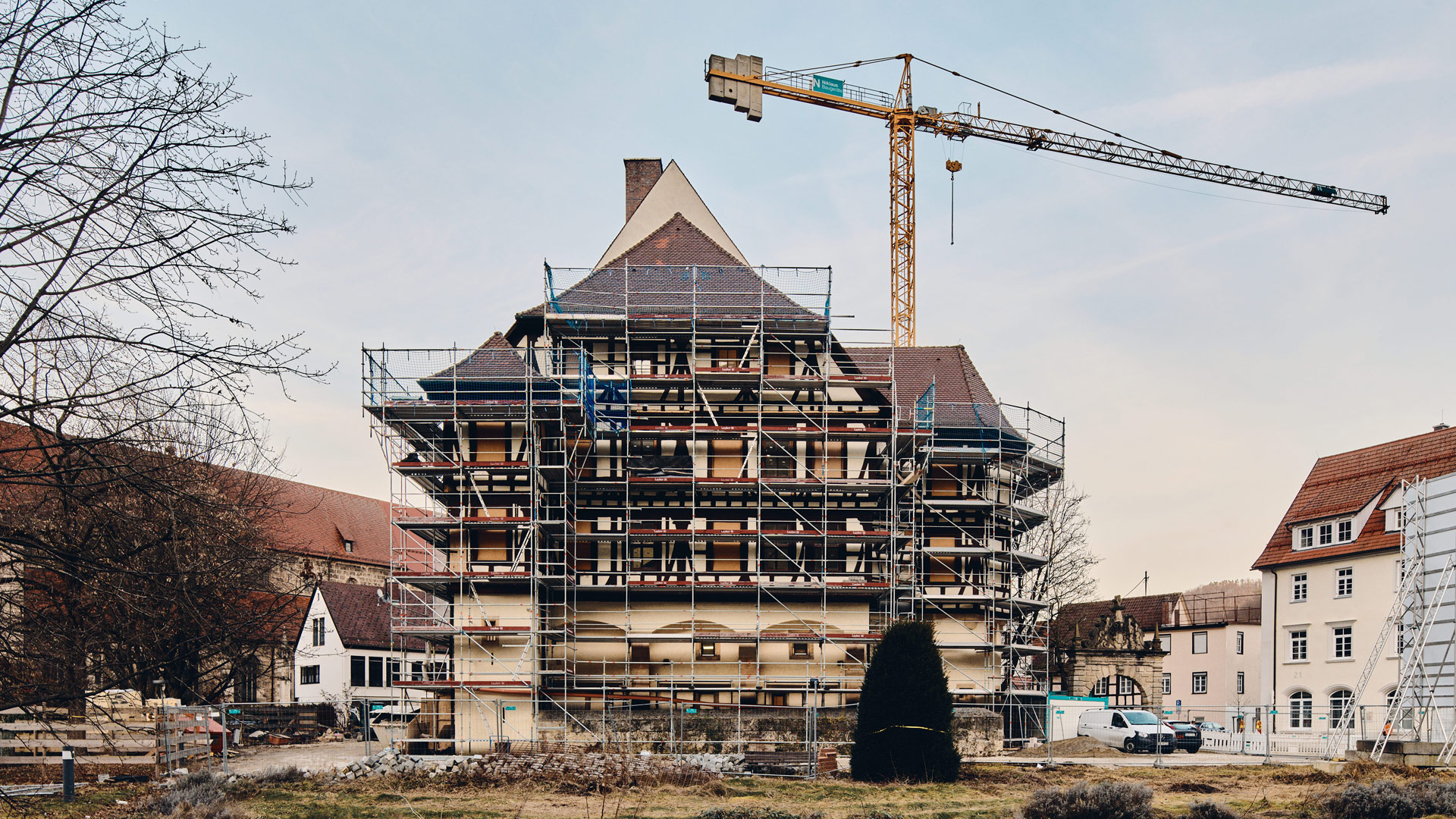 Ein eingerüstetes, historisches Gebäude inmitten einer Bebauung, dahinter ein Turmdrehkran.